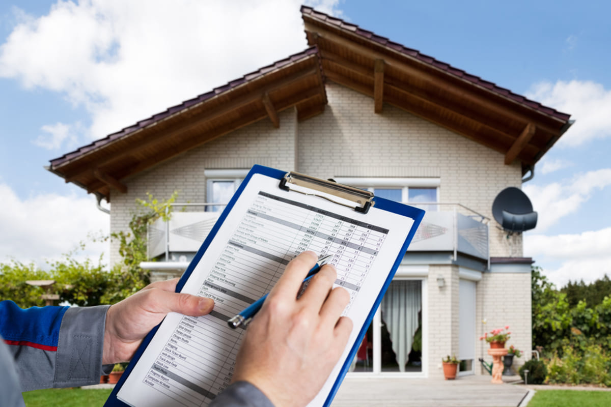 Close-up of hands with a checklist on a clipboard in front of a house, property management inspection concept