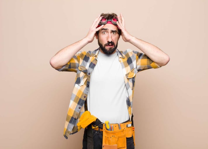 Young housekeeper man feeling horrified and shocked, raising hands to head and panicking at a mistake against flat wall