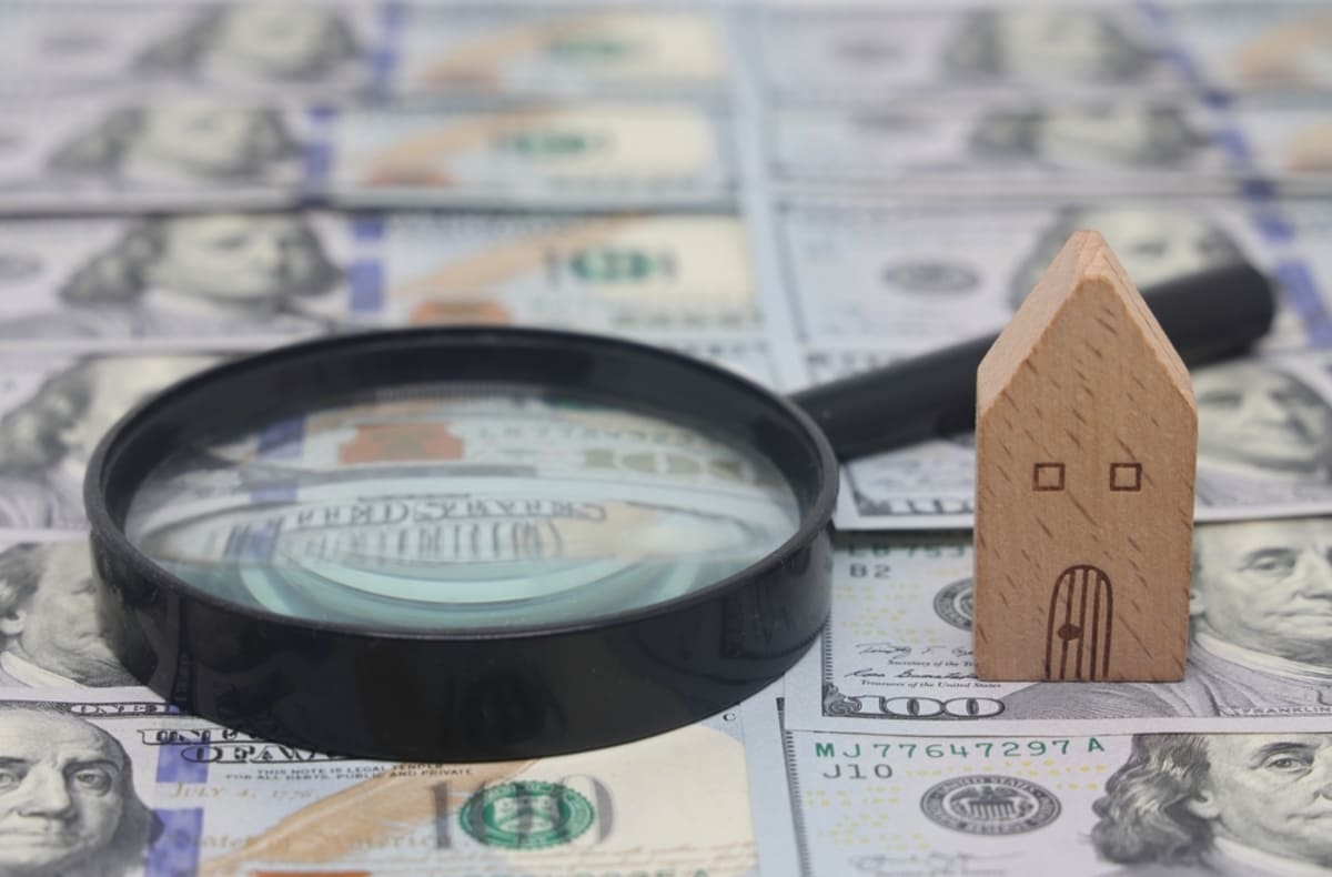 House model and magnifying glass on a background of dollar bills