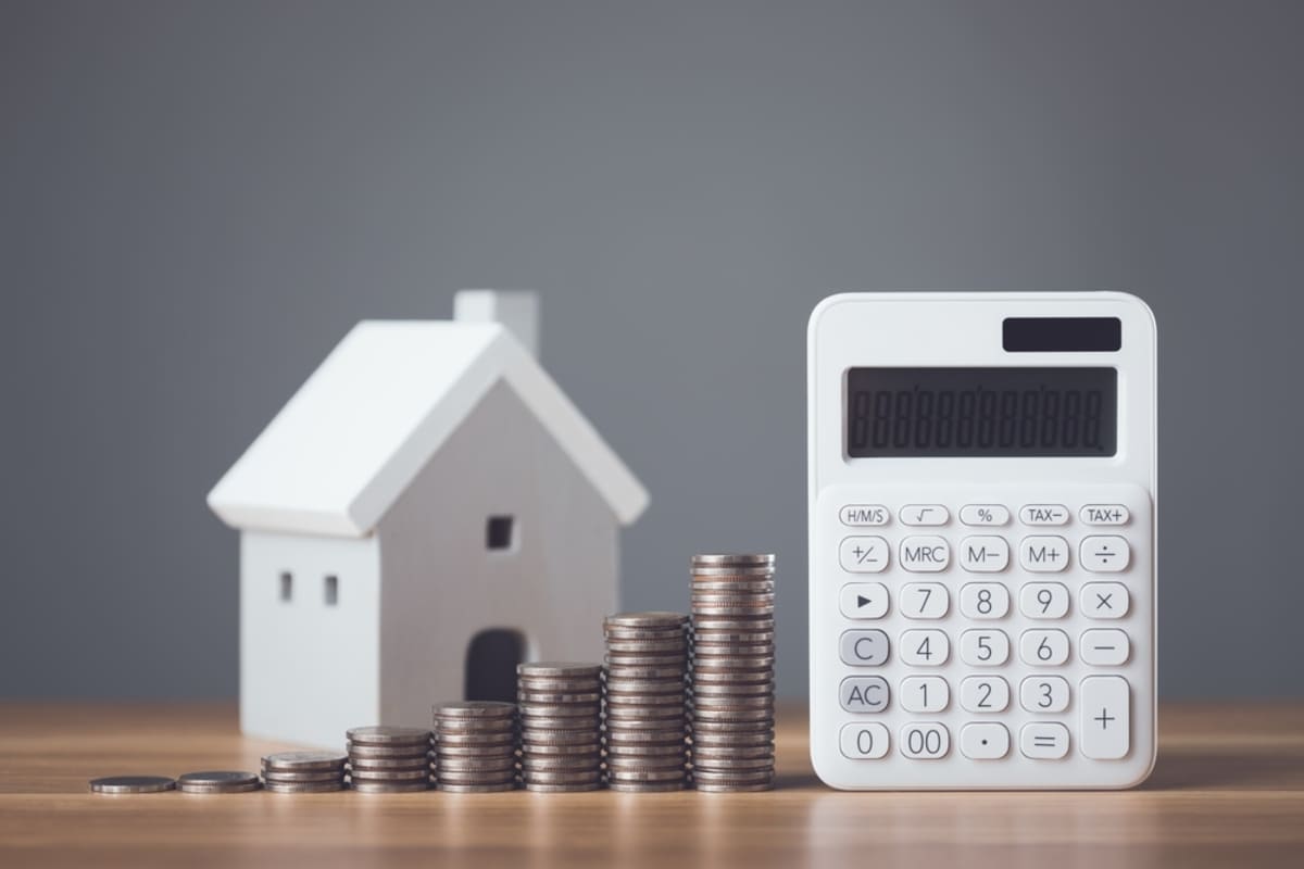 White model house by calculator and coins representing expense management