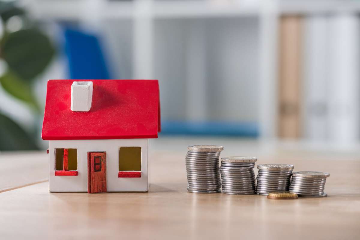 House model near stacks of golden and silver coins on wooden table