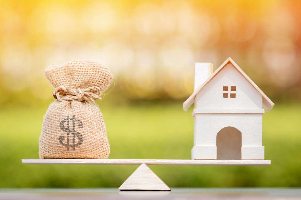 Home and money bag on scales with balance, owning rental properties concept.