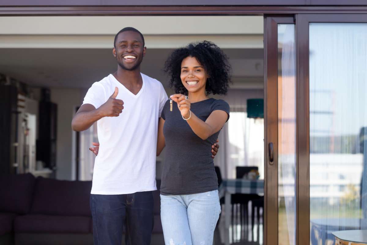 Happy couple standing in front of a house with keys, Philadelphia property management concept.